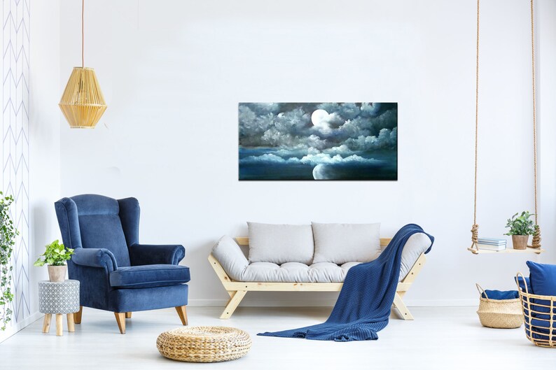 May include: A painting of a full moon shining through dark clouds in a night sky. The moon is white and the clouds are dark gray. The sky is a deep blue. The painting is framed and hanging on a white wall.