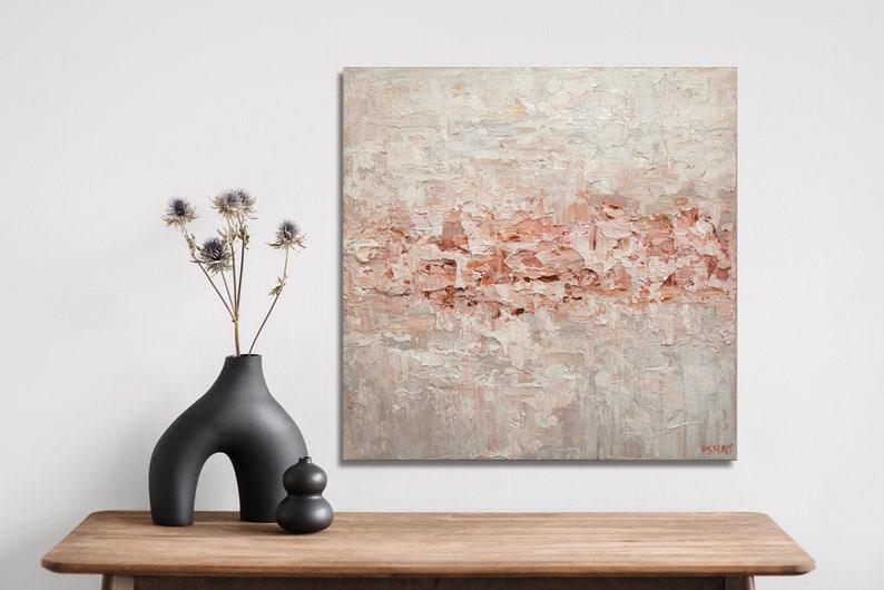 May include: Abstract painting with a textured, layered look. The painting features a light pink and white color scheme with a subtle hint of gray. The painting is framed and hanging on a white wall.