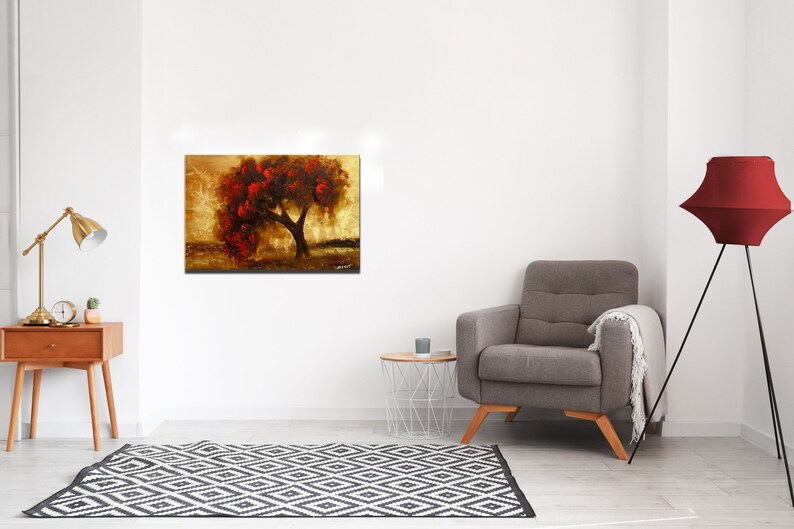 May include: A painting of a tree with red leaves against a gold background. The tree is in the center of the painting and is surrounded by a golden field. The painting is framed and hanging on a white wall.