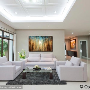 May include: Abstract painting with blue, brown, and gold hues depicting a forest scene. The painting is hanging on a wall in a living room with white furniture and a large window.