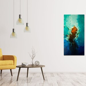 May include: Abstract painting with blue, green, and orange colors. The painting is hanging on a white wall in a living room setting with a yellow armchair and a coffee table.