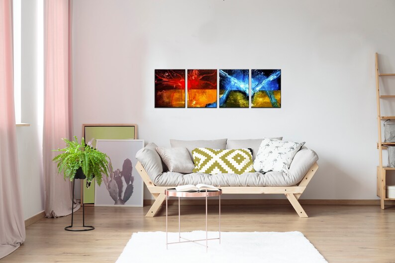 May include: A set of four abstract art prints featuring a mix of red, orange, yellow, and blue colors. The prints are arranged in a row on a white wall above a light-colored couch.