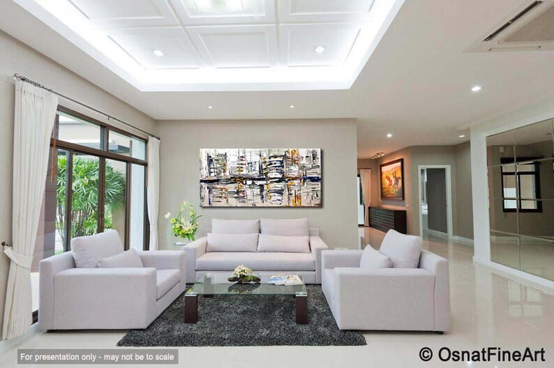 May include: Abstract painting in shades of white, gray, and black with hints of yellow and blue. The painting is hanging on a wall in a living room with white couches and a glass coffee table.