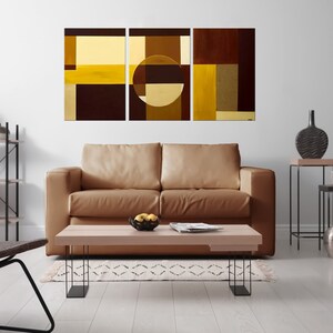 May include: A living room interior with a brown leather sofa, a coffee table, and a three-piece abstract art print featuring geometric shapes in shades of brown and yellow.