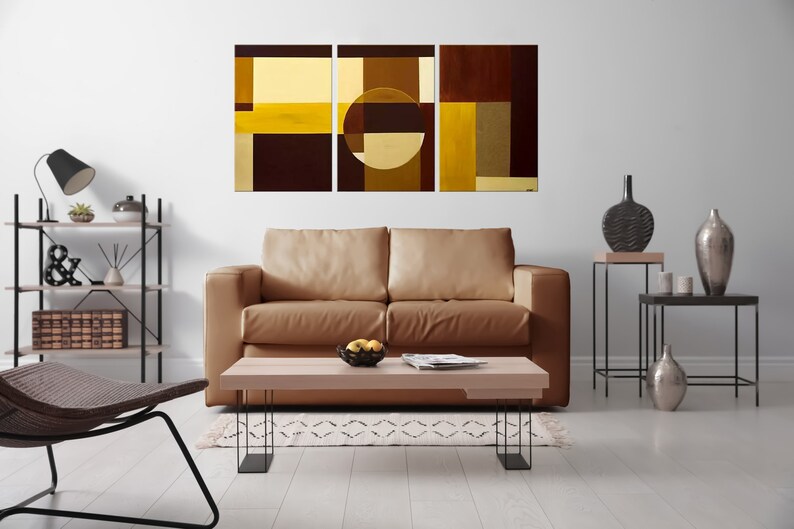 May include: A living room interior with a brown leather sofa, a coffee table, and a three-piece abstract art print featuring geometric shapes in shades of brown and yellow.