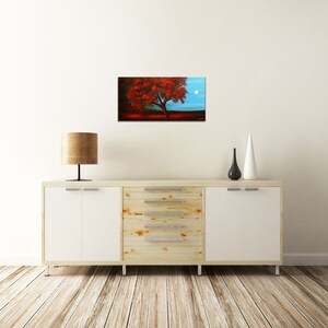 May include: A painting of a red tree with a full moon in the background. The tree is in the foreground and the moon is in the upper right corner of the painting. The sky is a light blue color.