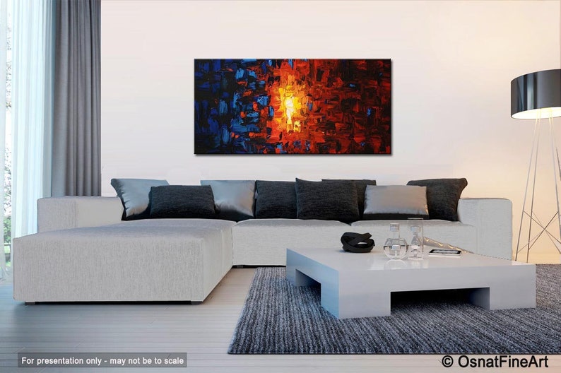 May include: Abstract painting with blue, red, and orange colors. The painting is hanging on a white wall above a white sectional sofa with gray pillows. A white coffee table with a black bowl and clear glasses sits in front of the sofa.