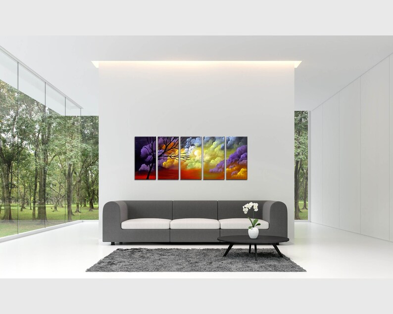 May include: A five-piece abstract art print set featuring a colorful sunset scene with a silhouette of a tree. The print set is displayed on a gray sofa in a modern living room.
