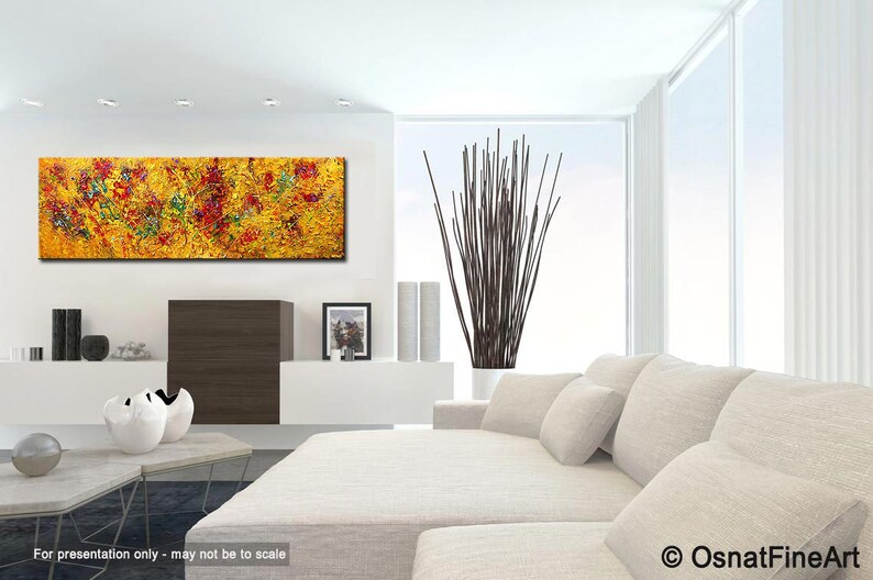 May include: Abstract painting with a yellow background and red, green, and blue accents. The painting is displayed in a modern living room with a white couch and a vase of brown branches.