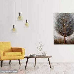 May include: A textured abstract painting of a tree in shades of gold, brown, and gray. The painting is displayed on a white wall in a living room setting with a yellow armchair and a coffee table.