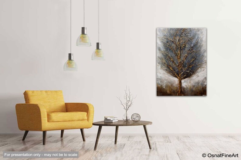 May include: A textured abstract painting of a tree in shades of gold, brown, and gray. The painting is displayed on a white wall in a living room setting with a yellow armchair and a coffee table.