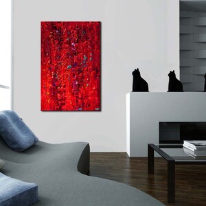 May include: Abstract painting in shades of red, with hints of blue and purple, hanging on a white wall in a modern living room. The painting is above a white fireplace with four black cat figurines on the mantel.