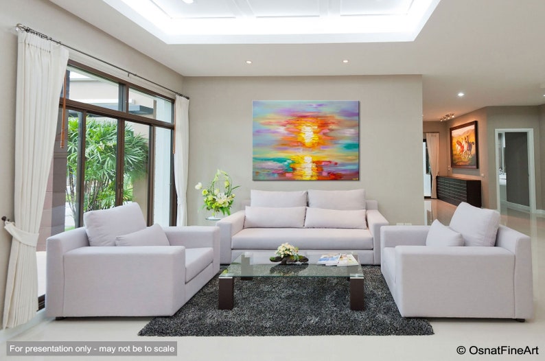 May include: A colorful abstract painting of a sunset over water, hanging on a wall in a living room with white couches and a glass coffee table.