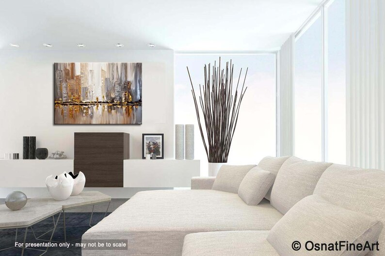 May include: Abstract cityscape painting with gold, brown, and gray tones. The painting is hanging on a white wall in a modern living room with a white couch and a vase of brown branches.