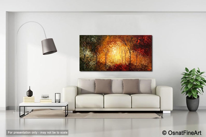 May include: A painting of a forest scene with trees in shades of green, yellow, orange, and red. The trees are illuminated by a bright light in the center of the painting. The painting is displayed on a white wall in a living room setting.