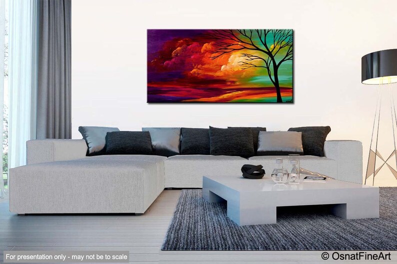May include: Abstract painting of a tree with a colorful sunset sky in the background. The painting is displayed on a white wall above a white couch with gray pillows.