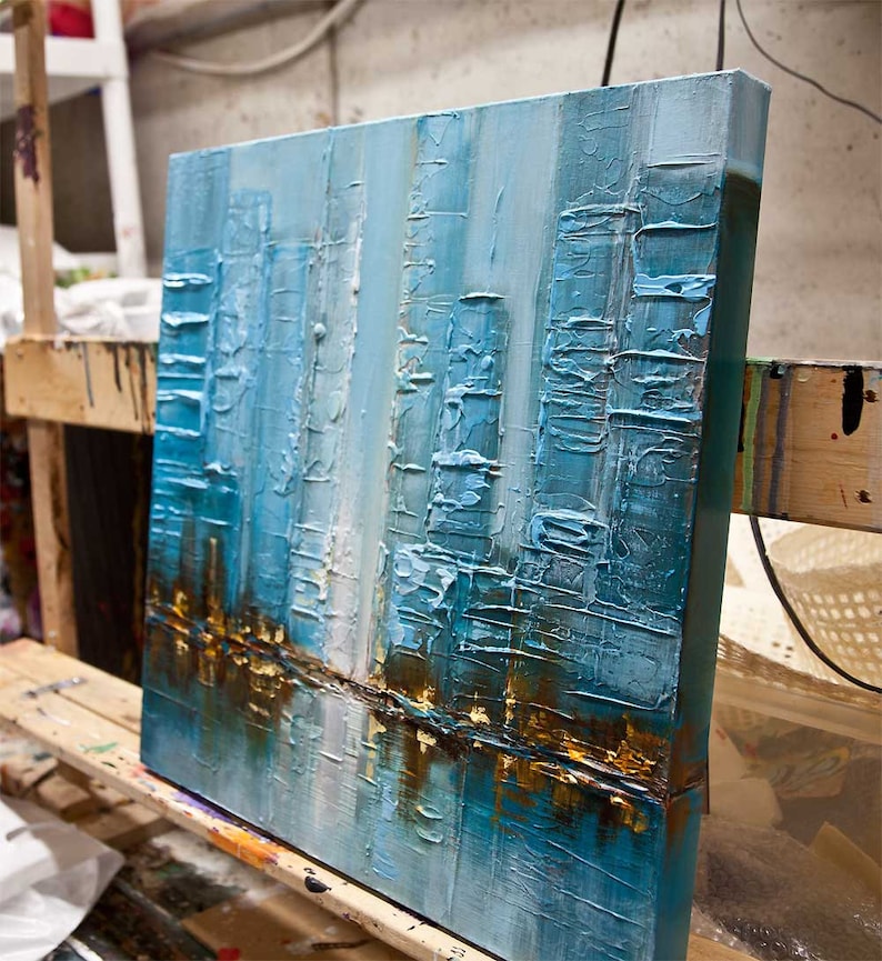 May include: Abstract painting on canvas with a textured surface. The painting features a cityscape with tall buildings in shades of blue, white, and gold.