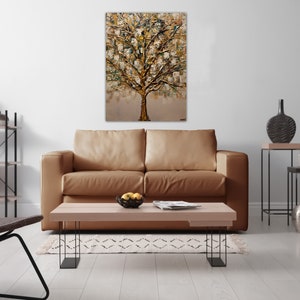 May include: A living room interior design with a brown leather sofa, a coffee table, a black metal shelf, and a painting of a gold tree on the wall.