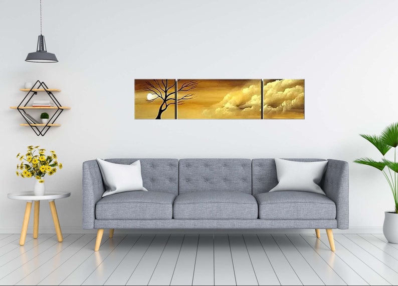 May include: A three-piece canvas wall art set featuring a silhouette of a tree against a sunset sky with clouds. The artwork is in shades of gold, brown, and white.