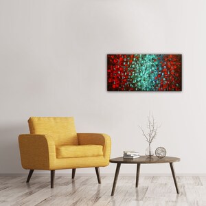 May include: Abstract painting with a red and teal color scheme. The painting is made up of small squares of color, creating a textured effect. The painting is hanging on a white wall above a yellow armchair and a coffee table.