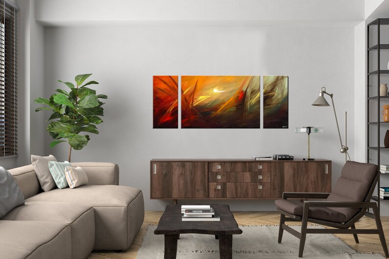 May include: Abstract art print in three panels, featuring a sunset scene with orange, yellow, and brown hues. The panels are hung on a white wall above a brown wooden cabinet.