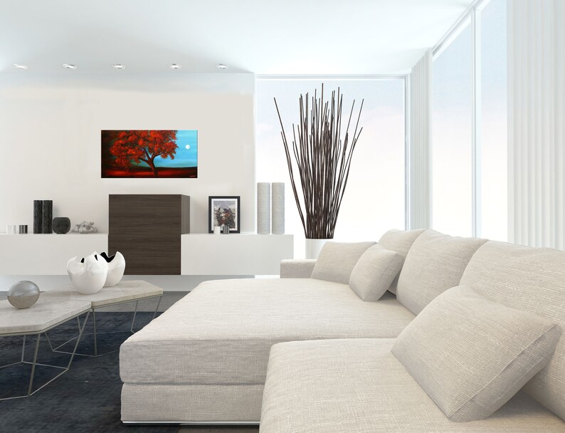 May include: A white sectional sofa with multiple pillows in a modern living room. A painting of a red tree with a full moon in the background hangs on the wall above a dark brown cabinet.
