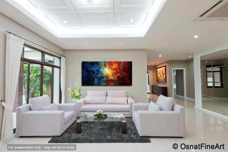 May include: Abstract painting with blue, orange, and yellow hues. The painting is hanging on a wall in a living room with white couches and a coffee table.