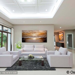 May include: A large abstract painting of a sunset over a body of water hangs on a wall in a living room. The painting is in shades of gold, brown, and white. The living room is decorated with white furniture and a gray rug.