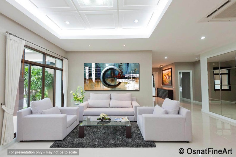 May include: Abstract painting with a large circle in the center, featuring shades of blue, gray, and white. The painting is displayed on a wall in a living room with white couches and a coffee table.