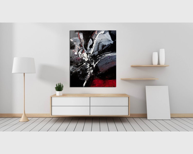 May include: Abstract painting with black, white, and red paint splatters and brushstrokes. The painting is framed and hanging on a white wall above a wooden dresser.