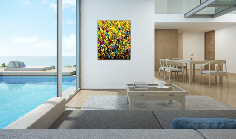 May include: Abstract painting of a field of colorful flowers in shades of yellow, blue, green, and purple. The painting is framed and hanging on a white wall in a modern living room.
