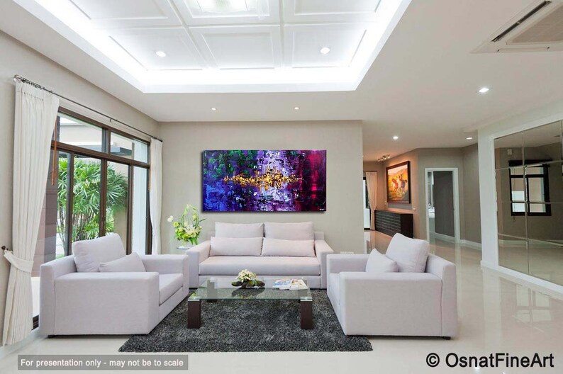 May include: Abstract painting in shades of purple, green, and gold, hanging on a wall in a modern living room with white couches and a coffee table.