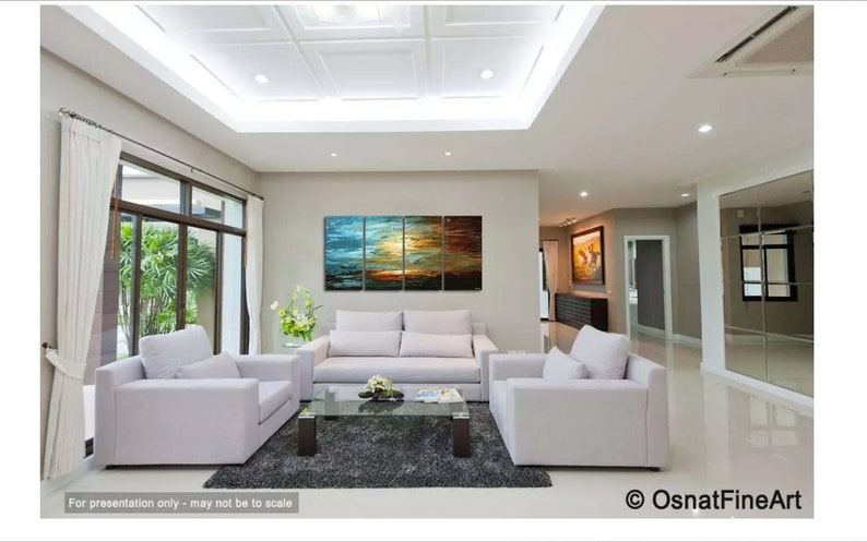 May include: A living room interior design featuring a multi-panel abstract painting with blue, green, orange, and brown hues. The painting is hung above a white sofa with two matching armchairs. The room has a modern aesthetic with a grey rug and a glass coffee table.