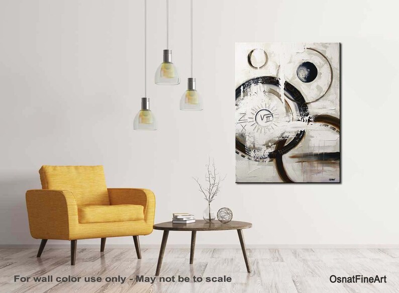 May include: Abstract painting with black and white circles and lines on a white background. The painting has a brown and white sun with Roman numerals in the center. The painting is hanging on a white wall in a living room setting.