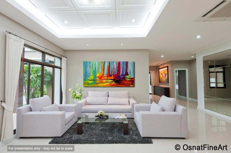 May include: Abstract painting of colorful vertical lines with a yellow, orange, and green base. The painting is hanging on a wall in a living room with white couches and a glass coffee table.
