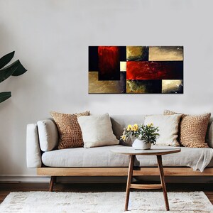 May include: Abstract painting with geometric shapes in shades of red, gold, black, and brown. The painting is displayed on a wall above a couch with pillows and a coffee table.