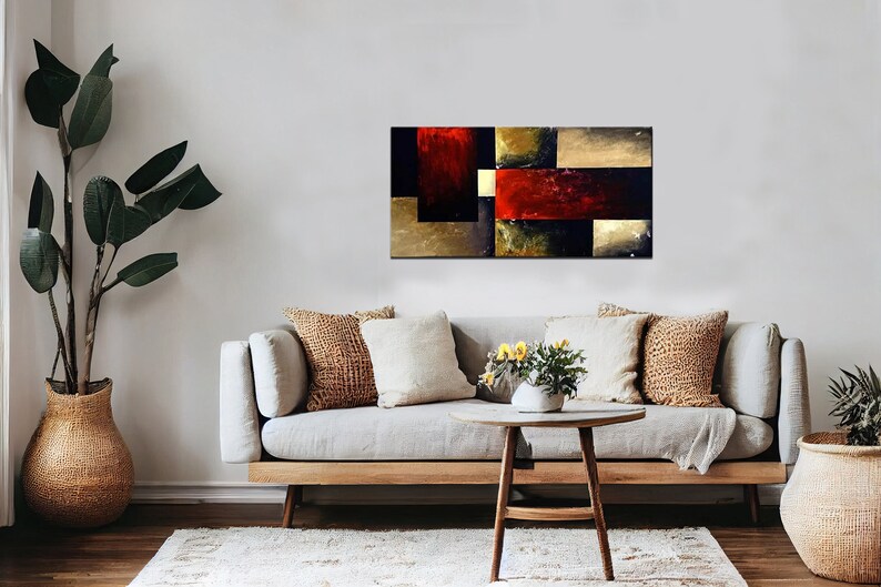 May include: Abstract painting with geometric shapes in shades of red, gold, black, and brown. The painting is displayed on a wall above a couch with pillows and a coffee table.