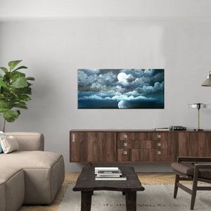May include: A painting of a full moon in a dark blue sky with white clouds. The moon is surrounded by clouds and the sky is dark blue. The painting is framed and hanging on a wall in a living room.