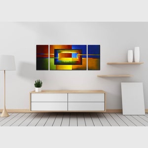 May include: Abstract art print with a geometric design in shades of blue, green, yellow, orange, and red. The print is divided into three panels and features a central square with a smaller square inside.