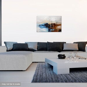 May include: Abstract painting with shades of blue, brown, and white. The painting is hanging on a white wall above a gray sectional sofa with black pillows. The sofa is in a living room setting with a gray rug and a white coffee table.
