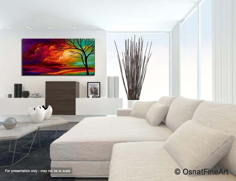 May include: Abstract painting of a tree with a colorful sunset sky in the background. The painting is displayed on a wall in a living room setting with a white couch and a coffee table.