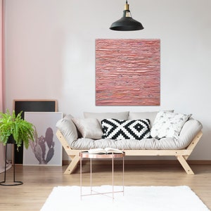 May include: A light pink abstract painting with horizontal brushstrokes hangs above a light beige sofa with black and white patterned pillows. The sofa is in a living room with a potted fern plant, a wooden ladder shelf, and a small round coffee table.
