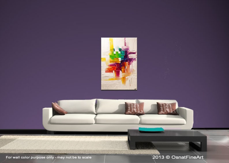 May include: Abstract painting with a white background and colorful geometric shapes in shades of red, orange, yellow, green, blue, and purple. The painting is hanging on a purple wall above a white couch with brown throw pillows.