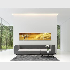 May include: A three-piece canvas wall art set featuring a sunset scene with a silhouette of a tree and clouds. The artwork is displayed above a gray sofa in a modern living room.