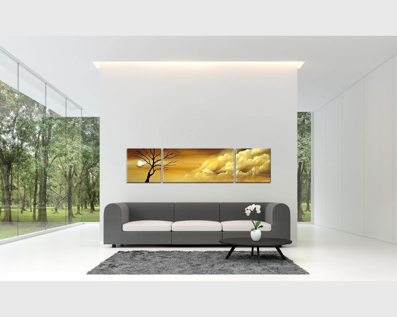 May include: A three-piece canvas wall art set featuring a sunset scene with a silhouette of a tree and clouds. The artwork is displayed above a gray sofa in a modern living room.