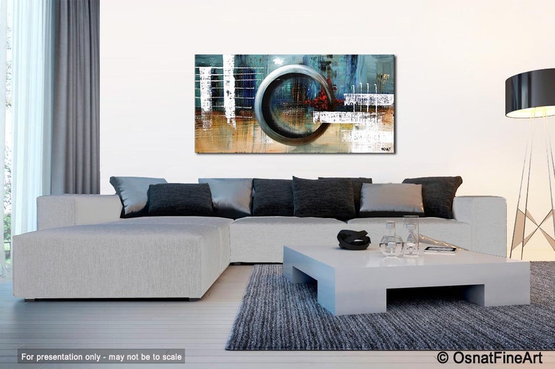 May include: Abstract painting with a large, circular, gray shape in the center. The painting is on a white wall in a living room setting with a gray sectional sofa and a white coffee table.