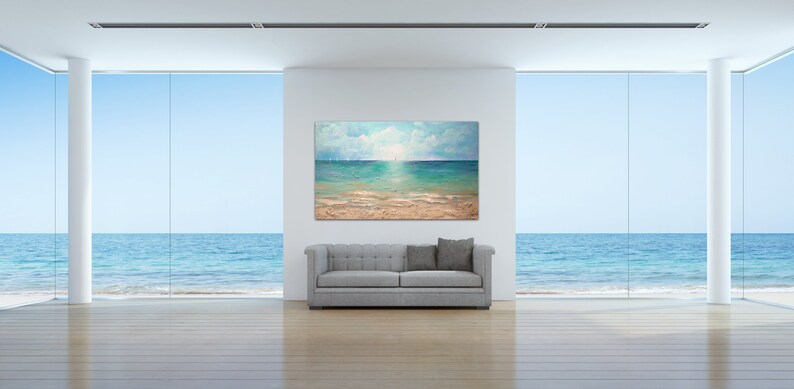 May include: A painting of a seascape with a blue sky, white clouds, and a turquoise ocean. The painting is hanging on a white wall in a room with large windows overlooking the ocean.