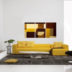 May include: A yellow sectional sofa with three pillows sits in front of a three-panel abstract painting with brown, yellow, and beige geometric shapes. A white oval coffee table sits in front of the sofa. A black chair sits to the right of the sofa. A small potted plant sits on a black metal stand to the left of the sofa.