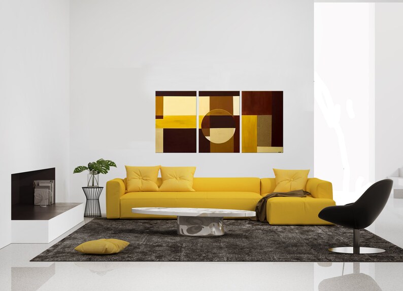 May include: A yellow sectional sofa with three pillows sits in front of a three-panel abstract painting with brown, yellow, and beige geometric shapes. A white oval coffee table sits in front of the sofa. A black chair sits to the right of the sofa. A small potted plant sits on a black metal stand to the left of the sofa.
