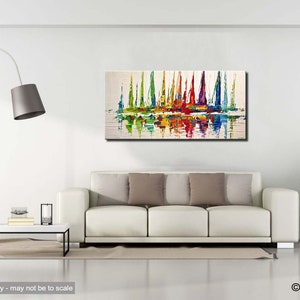 May include: Abstract painting of colorful sailboats on a white background with reflections in the water. The painting is framed and hanging on a white wall above a white couch.
